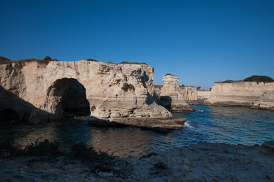 Rock formations by sea against clear blue sky