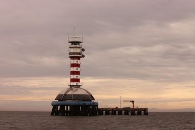 Lighthouse by sea against sky during sunset