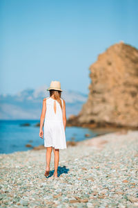 Rear view of woman standing on rock at beach against sky