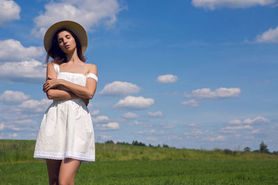 Young woman with long black hair stands in white dress and clothes straw hat is on the green field 