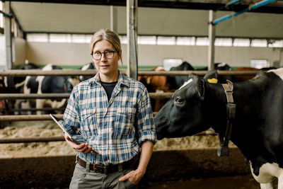 Female farmer with tablet pc standing by cow at cattle farm