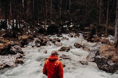 Rear view of man standing by river in forest during winter