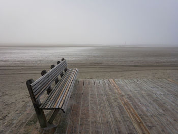 Empty bench by sea against clear sky