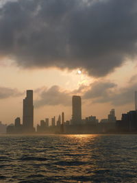 Sea by modern buildings against sky during sunset