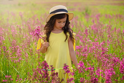 Romantic beautiful little girl walks in a flowering field, holds a bouquet of flowers