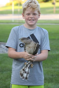 Smiling boy holding bird standing against blurred background