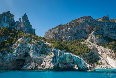 Rock formations in sea against clear blue sky