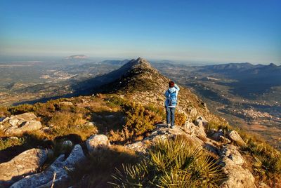 Rear view of mature woman with backpack standing on mountain against sky