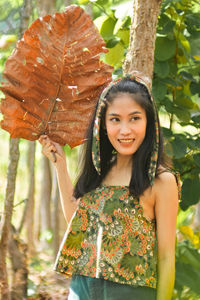 Portrait of smiling young woman standing against plants