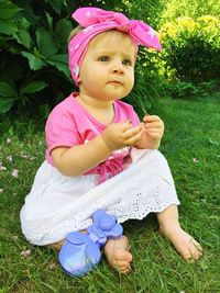 Full length of cute baby girl with bandana sitting on grassy field