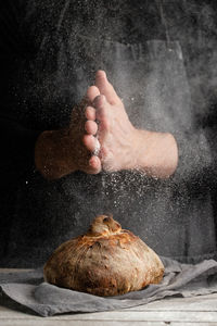 Unrecognizable chef in apron standing at table and decorating loaf of traditional bread with flour