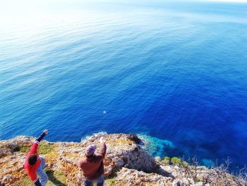 High angle view of men enjoying on rock formation over sea