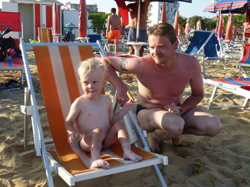 Shirtless father with son looking away at beach