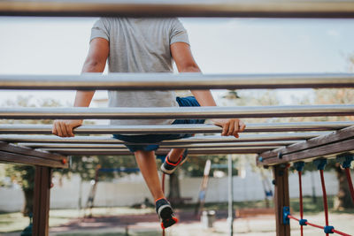 Low section of man sitting on monkey bars in playground