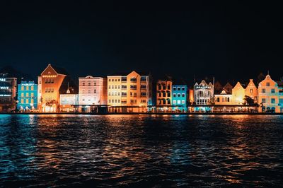 Buildings by river against sky at night