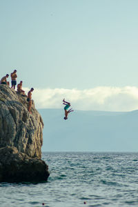 People jumping on rock in sea against sky