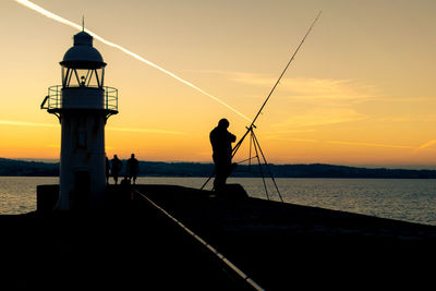 Silhouette man fishing on beach against sky during sunset