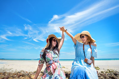 Excited women wearing sunglasses at beach against sky