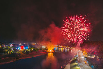 Firework display over illuminated city against sky at night