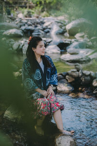 Young woman sitting on rock by water