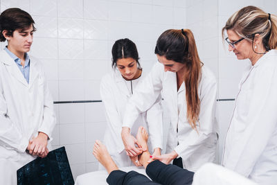 Two doctors are examining the leg of a patient that is lying on a stretcher on an hospital room while another is holding an x-ray