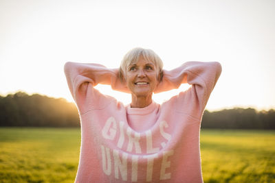 Portrait of confident senior woman standing on rural meadow at sunset