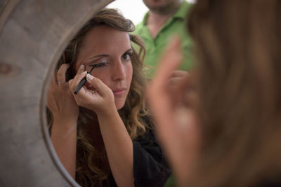 Close-up of woman applying eyeliner while looking in mirror