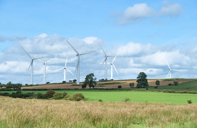 Wind turbines on field against cloudy sky