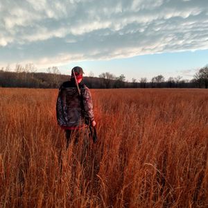 Rear view of hunter with gun standing at grassy field