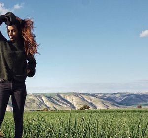 Young woman with hand in hair standing on agricultural field against sky