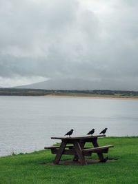 Empty bench by lake against sky