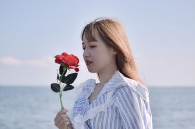 Midsection of woman holding flowering plant against sea