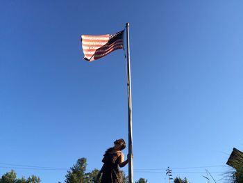 Low angle view of young woman looking at american flag against clear sky