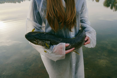 Midsection of young woman holding fish while standing in lake