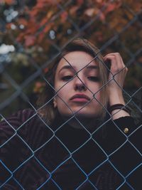 Portrait of young woman looking through chainlink fence