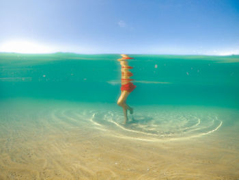 Underwater shot of female in red swimsuit in turquoise water standing on clear sandy bottom of lake