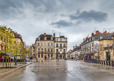 Wet street amidst buildings against sky during rainy season