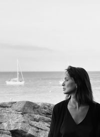 Portrait of young woman standing at beach against clear sky black and white 