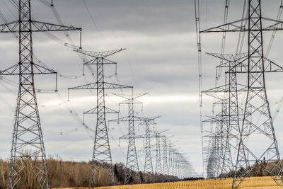 Low angle view of electricity pylon against cloudy sky