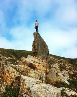 Low angle view of man standing on rock against sky