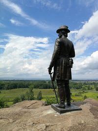 Rear view of statue on field against sky