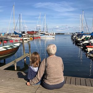 Rear view of grandmother and granddaughter sitting on pier at harbor