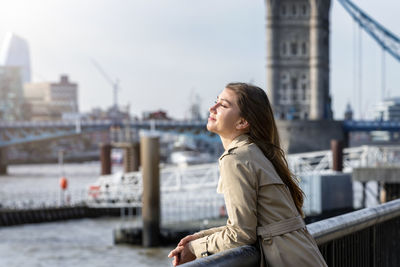 Young woman standing with eyes closed by railing in city