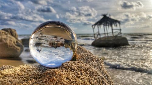 Close-up of crystal ball on beach against sky