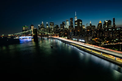 Illuminated bridge over river by buildings against sky at night