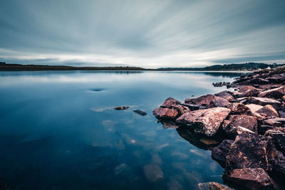 Scenic view of sea by rocks against cloudy sky