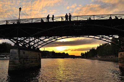 Silhouette bridge over river against sky during sunset