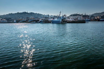 Sailboats moored in sea against sky in city
