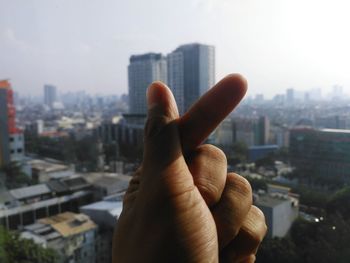 Cropped hand of person gesturing against buildings and sky in city