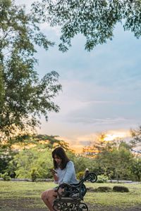 Woman sitting on field against sky during sunset